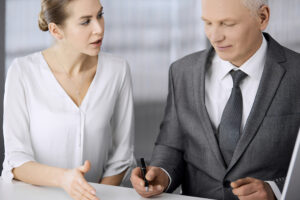 Elderly businessman and woman sitting and communicating in office. Adult business people or lawyers working together as a partners and colleagues at meeting. Teamwork and cooperation concept